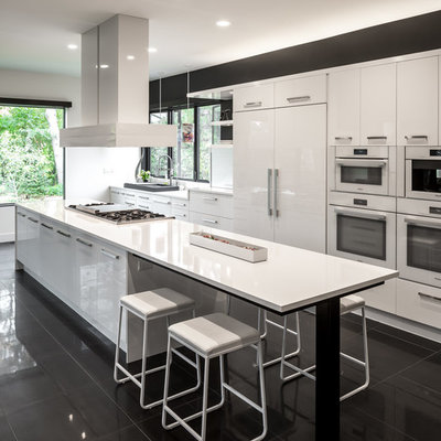 Open concept kitchen - huge contemporary galley porcelain tile and black floor open concept kitchen idea in Minneapolis with flat-panel cabinets, white cabinets, white appliances, an island, a single-bowl sink, quartz countertops, white backsplash and white countertops