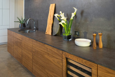 Photo of a medium sized modern l-shaped open plan kitchen in Oklahoma City with a submerged sink, flat-panel cabinets, engineered stone countertops, black splashback, white appliances, concrete flooring and an island.