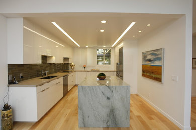 This is an example of a large modern u-shaped kitchen/diner in Santa Barbara with a submerged sink, flat-panel cabinets, white cabinets, marble worktops, black splashback, ceramic splashback, stainless steel appliances, light hardwood flooring and an island.