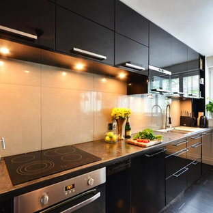 Photo of a small modern galley open plan kitchen in London with a drop-in sink, flat-panel cabinets, black cabinets, concrete benchtops, grey splashback, porcelain splashback, panelled appliances and bamboo floors.