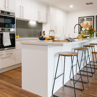 Large contemporary u-shaped kitchen in Melbourne with a double-bowl sink, open cabinets, white cabinets, quartz benchtops, metallic splashback, glass sheet splashback, stainless steel appliances, medium hardwood floors, with island and beige benchtop.