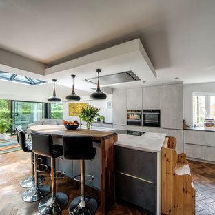 Ispirazione per una grande cucina moderna con ante lisce, ante grigie, elettrodomestici in acciaio inossidabile, pavimento in legno massello medio, isola, pavimento marrone e top bianco