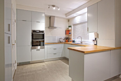 This is an example of a medium sized contemporary l-shaped kitchen/diner in Limerick with a single-bowl sink, flat-panel cabinets, blue cabinets, wood worktops, glass sheet splashback, integrated appliances, lino flooring and no island.