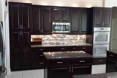 Example of a mid-sized minimalist l-shaped porcelain tile eat-in kitchen design in Tampa with an undermount sink, raised-panel cabinets, black cabinets, granite countertops, gray backsplash, mosaic tile backsplash, stainless steel appliances and an island