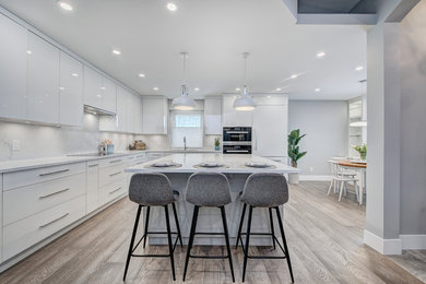 Example of a mid-sized trendy u-shaped light wood floor and beige floor eat-in kitchen design in Calgary with an undermount sink, flat-panel cabinets, white cabinets, quartzite countertops, white backsplash, stone slab backsplash, paneled appliances, an island and white countertops