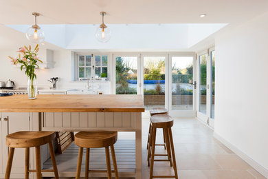 Inspiration for a large farmhouse l-shaped open plan kitchen in Kent with a belfast sink, shaker cabinets, grey cabinets, wood worktops, white splashback, stainless steel appliances, limestone flooring and an island.