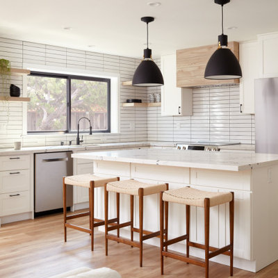 Inspiration for a transitional l-shaped medium tone wood floor and brown floor open concept kitchen remodel in San Francisco with an undermount sink, shaker cabinets, white cabinets, white backsplash, stainless steel appliances, an island and white countertops