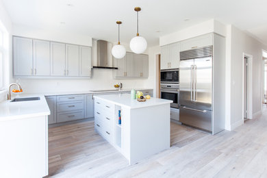 Example of a large trendy light wood floor kitchen design in Toronto with an undermount sink, shaker cabinets, gray cabinets, quartz countertops, white backsplash, subway tile backsplash, stainless steel appliances and an island