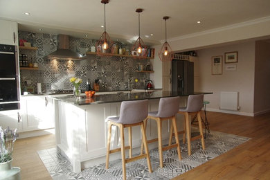 Inspiration for a large modern grey and white single-wall kitchen/diner in Cardiff with a belfast sink, shaker cabinets, white cabinets, quartz worktops, multi-coloured splashback, ceramic splashback, stainless steel appliances, laminate floors, an island, multi-coloured floors, black worktops and a feature wall.