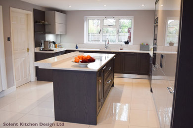 Design ideas for a medium sized modern kitchen/diner in Hampshire with flat-panel cabinets, grey cabinets, engineered stone countertops, white splashback, glass sheet splashback, black appliances, porcelain flooring, an island, white floors and white worktops.