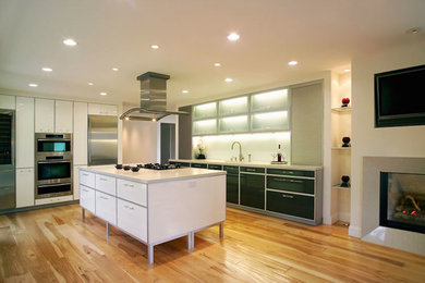 Diseño de cocina minimalista extra grande con armarios con paneles lisos, puertas de armario blancas, electrodomésticos de acero inoxidable, suelo de madera clara y una isla