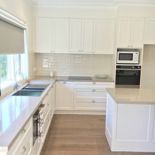 This is an example of a large traditional l-shaped kitchen in Melbourne with a double-bowl sink, shaker cabinets, limestone benchtops, beige splashback, subway tile splashback, stainless steel appliances, dark hardwood floors and with island.