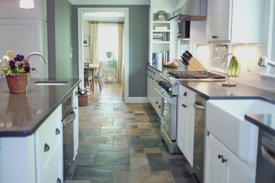 Example of a mid-sized minimalist galley slate floor enclosed kitchen design in New York with a farmhouse sink, shaker cabinets, white cabinets, quartz countertops, white backsplash, subway tile backsplash, stainless steel appliances and an island