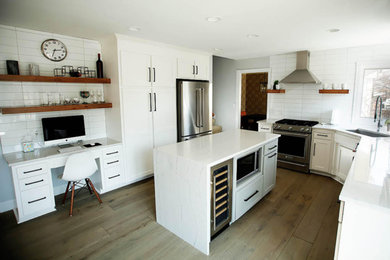 Inredning av ett klassiskt mellanstort vit vitt u-kök, med en undermonterad diskho, skåp i shakerstil, vita skåp, bänkskiva i kvartsit, vitt stänkskydd, stänkskydd i keramik, rostfria vitvaror, mellanmörkt trägolv, en köksö och brunt golv