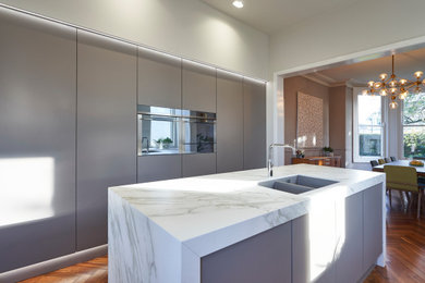 Photo of a large modern galley open plan kitchen in Other with a double-bowl sink, flat-panel cabinets, brown cabinets, engineered stone countertops, beige splashback, glass sheet splashback, stainless steel appliances, dark hardwood flooring, an island, brown floors and beige worktops.