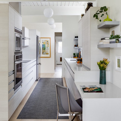 Enclosed kitchen - mid-sized 1950s galley light wood floor and beige floor enclosed kitchen idea in San Francisco with an undermount sink, flat-panel cabinets, stainless steel appliances, solid surface countertops, white cabinets, white countertops, multicolored backsplash and mosaic tile backsplash