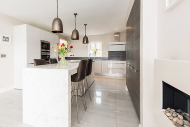 Bild på ett funkis kök och matrum, med släta luckor, vita skåp, marmorbänkskiva, rostfria vitvaror, klinkergolv i porslin och en köksö
