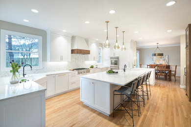 Example of a transitional u-shaped light wood floor and beige floor kitchen design in Portland with a farmhouse sink, shaker cabinets, white cabinets, white backsplash, mosaic tile backsplash, stainless steel appliances, an island and white countertops