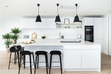 Cette image montre une cuisine parallèle design avec un placard à porte plane, des portes de placard blanches, une crédence blanche, un électroménager noir, îlot, un sol beige et un plan de travail blanc.