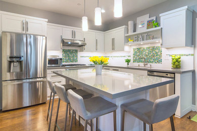 Example of a mid-sized minimalist l-shaped eat-in kitchen design in Orange County with a single-bowl sink, shaker cabinets, white cabinets, quartz countertops, white backsplash, glass tile backsplash, stainless steel appliances and an island