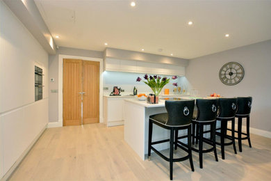 Photo of a medium sized modern l-shaped open plan kitchen in Other with an integrated sink, flat-panel cabinets, white cabinets, quartz worktops, black appliances, an island and white worktops.