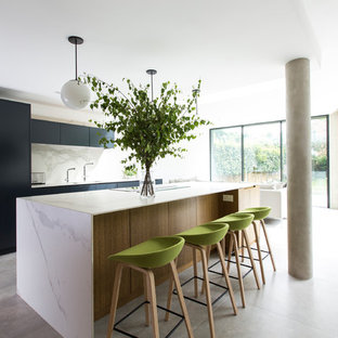 This is an example of an expansive modern galley open plan kitchen in London with flat-panel cabinets, black cabinets, marble worktops, white splashback, marble splashback, concrete flooring, an island, grey floors, a submerged sink and white worktops.