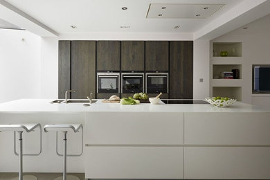 This is an example of a large contemporary single-wall kitchen/diner in London with a submerged sink, flat-panel cabinets, dark wood cabinets, composite countertops, stainless steel appliances, concrete flooring and an island.