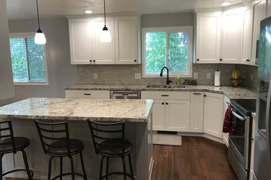 Mid-sized minimalist l-shaped medium tone wood floor and brown floor kitchen photo in Salt Lake City with an undermount sink, flat-panel cabinets, white cabinets, granite countertops, gray backsplash, stone tile backsplash, stainless steel appliances, an island and white countertops