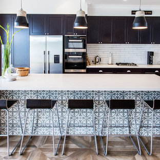 Photo of a mid-sized transitional l-shaped kitchen in Sydney with a drop-in sink, recessed-panel cabinets, black cabinets, white splashback, stainless steel appliances, light hardwood floors and with island.