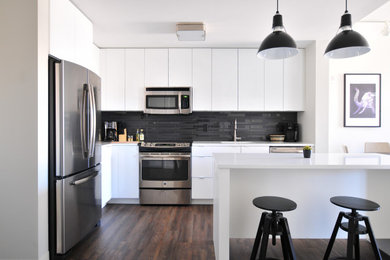 Inspiration for a mid-sized modern l-shaped dark wood floor and brown floor eat-in kitchen remodel in Orange County with an undermount sink, flat-panel cabinets, white cabinets, black backsplash, porcelain backsplash, stainless steel appliances, an island and white countertops