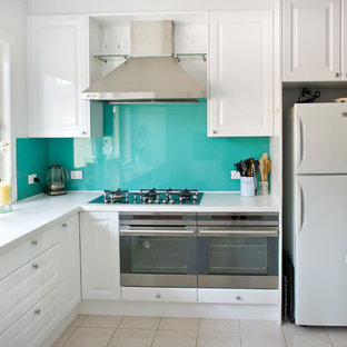 This is an example of a mid-sized contemporary u-shaped open plan kitchen in Melbourne with solid surface benchtops, glass sheet splashback, white cabinets, ceramic floors, with island, an integrated sink, raised-panel cabinets and stainless steel appliances.