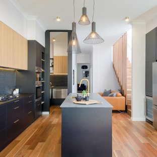 Contemporary u-shaped open plan kitchen in Sydney with an undermount sink, flat-panel cabinets, black cabinets, quartz benchtops, black splashback, mosaic tile splashback, stainless steel appliances, medium hardwood floors, with island, brown floor and black benchtop.