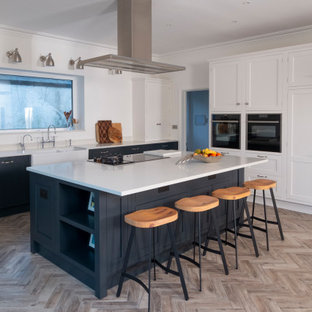 This is an example of a large classic l-shaped kitchen in Cardiff with a belfast sink, shaker cabinets, white cabinets, integrated appliances, an island, beige floors and white worktops.
