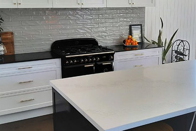 Exempel på ett stort klassiskt vit vitt kök, med skåp i shakerstil, vita skåp, bänkskiva i kvarts, stänkskydd i tunnelbanekakel, svarta vitvaror, mörkt trägolv, en köksö och brunt golv