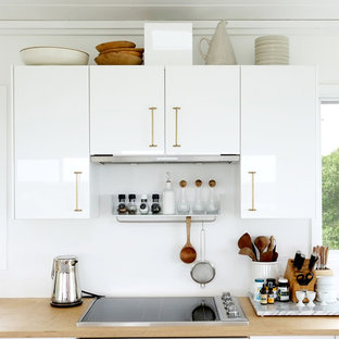 Contemporary kitchen remodeling - Trendy kitchen photo in New York with flat-panel cabinets, white cabinets, white backsplash, stainless steel appliances and wood countertops