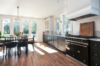 Inspiration for a large cottage galley medium tone wood floor and brown floor enclosed kitchen remodel in New York with a farmhouse sink, shaker cabinets, black cabinets, marble countertops, black appliances, an island and white countertops