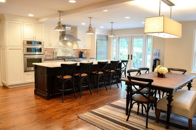 Example of a large classic l-shaped medium tone wood floor eat-in kitchen design in Newark with a farmhouse sink, recessed-panel cabinets, beige cabinets, concrete countertops, multicolored backsplash, stone tile backsplash, stainless steel appliances and an island
