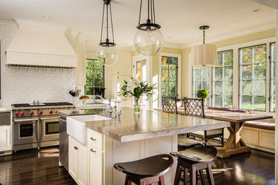 Example of a mid-sized classic l-shaped dark wood floor open concept kitchen design in Other with a farmhouse sink, white cabinets, marble countertops, white backsplash, ceramic backsplash, stainless steel appliances, an island and beaded inset cabinets