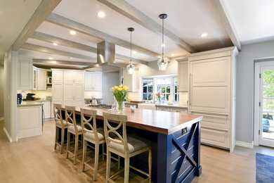 Example of a transitional u-shaped light wood floor open concept kitchen design in Santa Barbara with a farmhouse sink, flat-panel cabinets, white cabinets, granite countertops, white backsplash, stone tile backsplash, stainless steel appliances and an island