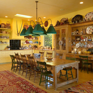 Foto de cocina comedor en L, ecléctica, con armarios con paneles lisos, puertas de armario amarillas, salpicadero negro y electrodomésticos negros