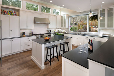 Photo of a large classic l-shaped kitchen in Santa Barbara with a submerged sink, recessed-panel cabinets, white cabinets, granite worktops, ceramic splashback, stainless steel appliances, light hardwood flooring and multiple islands.