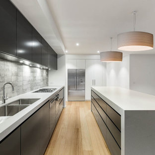 Inspiration for a modern l-shaped kitchen in Melbourne with an undermount sink, flat-panel cabinets, black cabinets, grey splashback, stainless steel appliances, light hardwood floors, with island, beige floor and white benchtop.