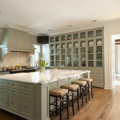 Inspiration for a mid-sized timeless u-shaped medium tone wood floor enclosed kitchen remodel in Dallas with glass-front cabinets, subway tile backsplash, green cabinets, a farmhouse sink, marble countertops, gray backsplash and an island