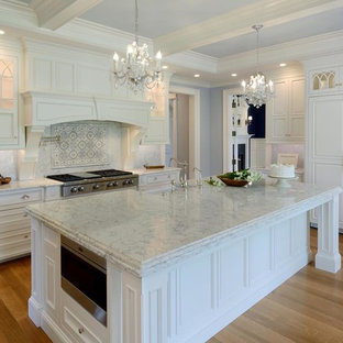 Photo of a large shabby-chic style l-shaped separate kitchen in Boston with a farmhouse sink, beaded inset cabinets, white cabinets, marble benchtops, grey splashback, mosaic tile splashback, panelled appliances, light hardwood floors, with island and brown floor.