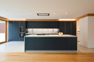 Photo of a large contemporary galley open plan kitchen in London with a built-in sink, flat-panel cabinets, blue cabinets, quartz worktops, grey splashback, stone slab splashback, stainless steel appliances, ceramic flooring, an island and grey worktops.