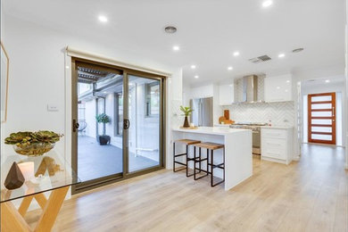 Example of a trendy galley laminate floor and brown floor eat-in kitchen design in Melbourne with a double-bowl sink, flat-panel cabinets, white cabinets, quartz countertops, white backsplash, ceramic backsplash, stainless steel appliances, no island and white countertops