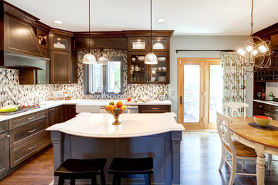 Inspiration for a medium sized traditional grey and cream l-shaped kitchen/diner in Minneapolis with a belfast sink, recessed-panel cabinets, dark wood cabinets, engineered stone countertops, blue splashback, glass tiled splashback, stainless steel appliances, medium hardwood flooring and an island.