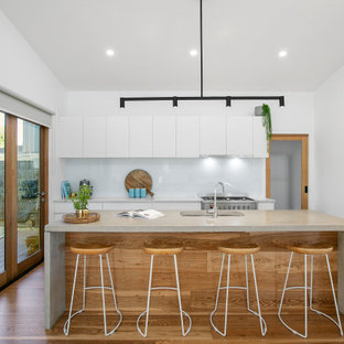 Mid-sized contemporary galley open plan kitchen in Melbourne with an undermount sink, flat-panel cabinets, white cabinets, concrete benchtops, white splashback, glass sheet splashback, stainless steel appliances, medium hardwood floors, with island, beige floor, grey benchtop and vaulted.
