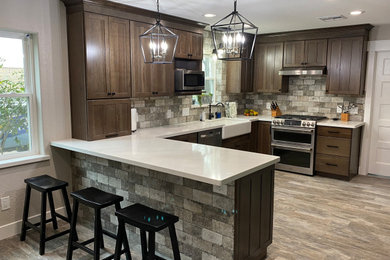 Example of a mid-sized arts and crafts u-shaped porcelain tile and gray floor eat-in kitchen design in Houston with a farmhouse sink, shaker cabinets, brown cabinets, wood countertops, gray backsplash, travertine backsplash, stainless steel appliances, a peninsula and white countertops
