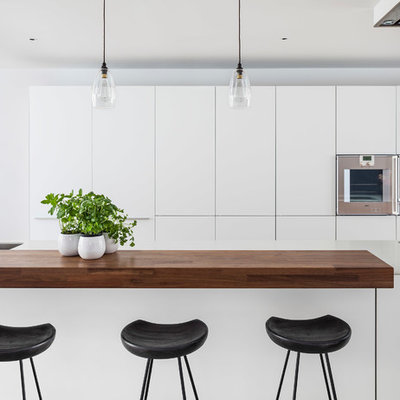 Kitchen - modern single-wall kitchen idea in London with flat-panel cabinets, white cabinets, an island, an undermount sink, solid surface countertops and stainless steel appliances